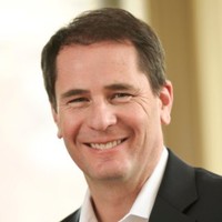 A man with short dark hair, wearing a black suit jacket and white shirt, smiling in a softly lit indoor setting, reflects confidence—ideal for roles in AI fraud detection or digital fraud prevention.